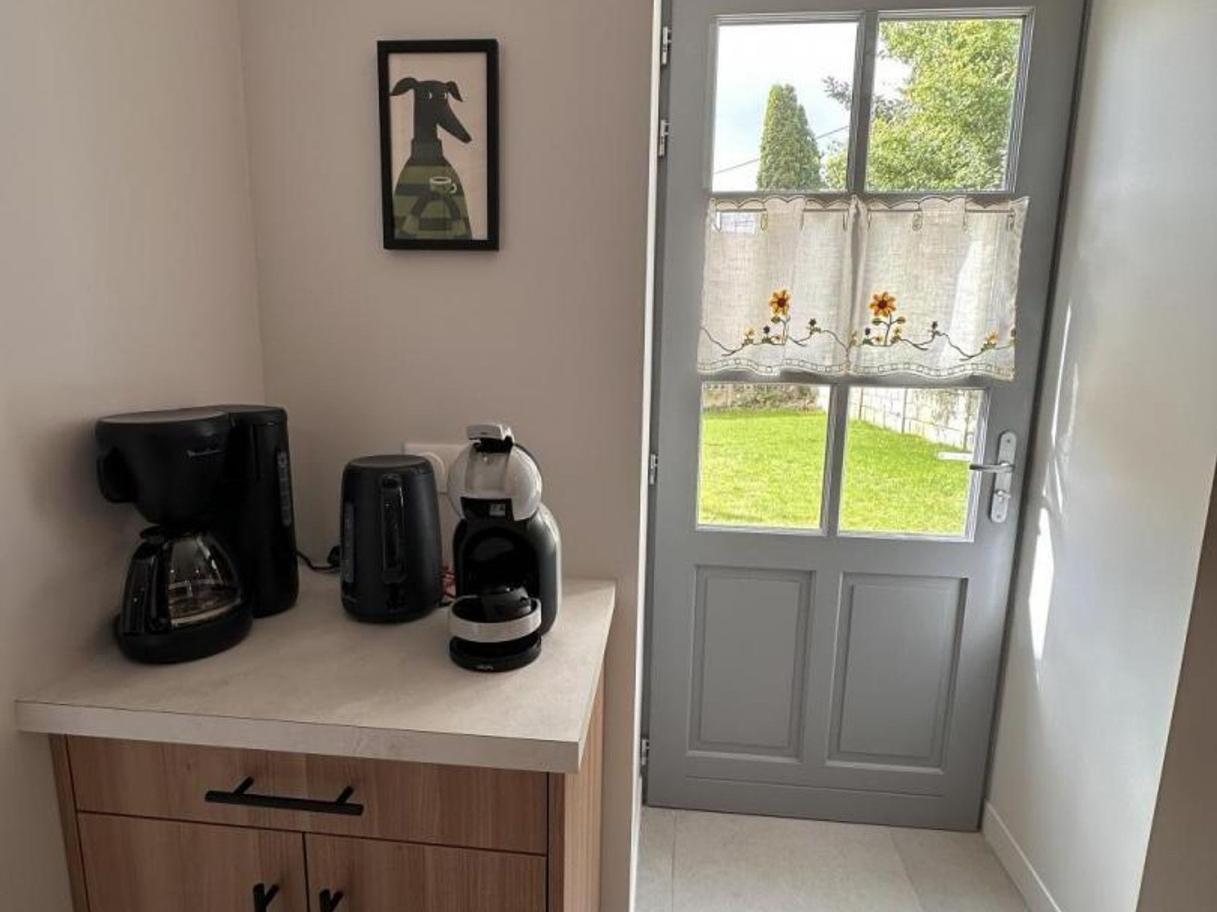 A kitchenette with a coffee maker, a kettle, and a framed picture on the wall.