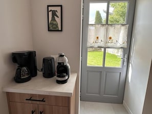 A kitchenette with a coffee maker, a kettle, and a framed picture on the wall.