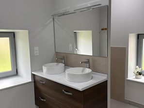 Casa de banho com duas pias redondas brancas, um espelho grande e uma janela.