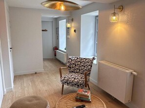 A room with a patterned armchair, a round table with books and a remote, a radiator, and a ceiling light fixture. - Independent house, pets welcome - 8 guests (La Celle)