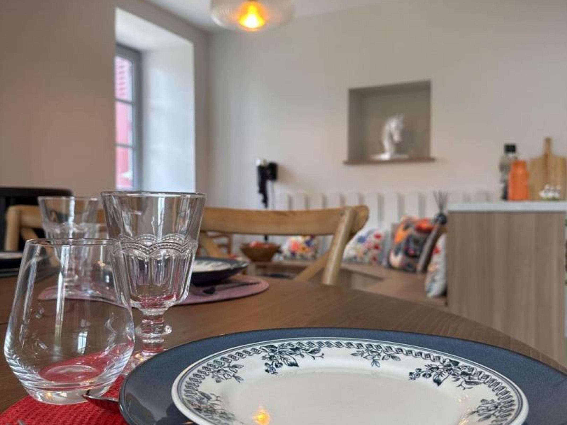 A dining table with a plate and glasses, a chair, and a window in the background.