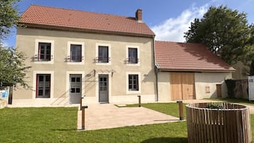 Een gebouw met twee verdiepingen, voorzien van een rood pannendak, een voordeur en een kleine tuin met een houten plantenbak.