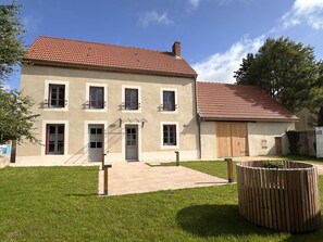 A two-story building with a red-tiled roof, a front door, and a small garden area with a wooden planter.