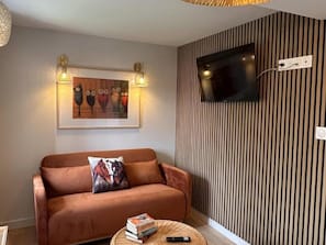 A living room with a brown sofa, a mounted TV, and a framed artwork above the sofa.