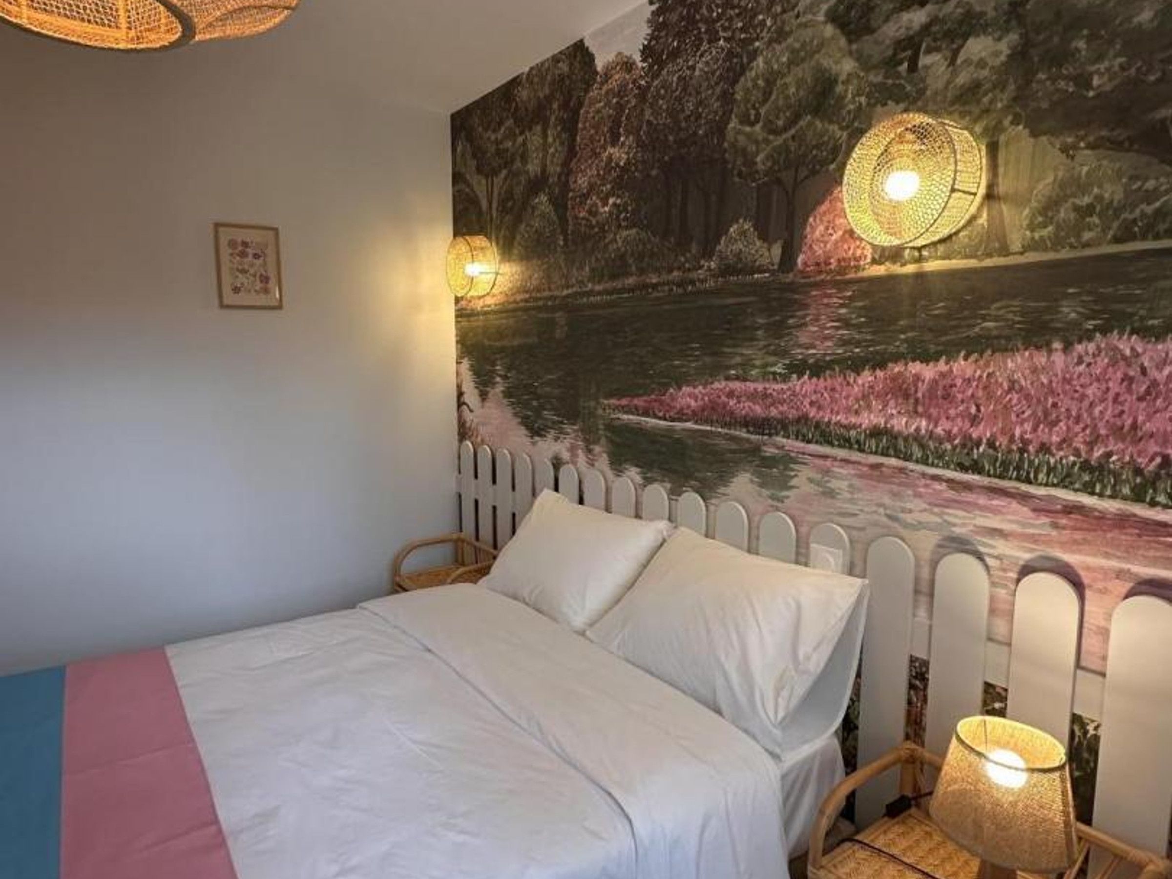 Un dormitorio con una cama, una lámpara de pared y un mural de un paisaje.
