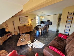 A living room with a brown leather sofa, a wooden coffee table, and a dining area with a table set for four. - Cozy apartment with mountain views - 6 guests (Saint-Gervais-les-Bains)