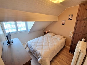 A bedroom with a sloped ceiling, a bed with a quilted duvet, a bedside table with a lamp, and a radiator. - Cozy apartment with mountain views - 6 guests (Saint-Gervais-les-Bains)