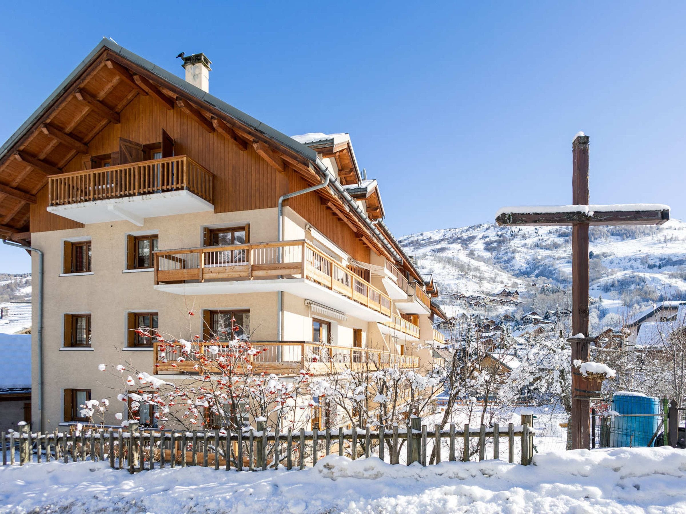 A multi-story wooden building with balconies, set against a snowy mountainous backdrop.