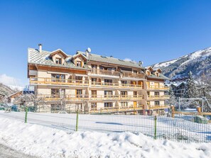 Een meerhoog hotel met balkons, een skipiste op de voorgrond en besneeuwde bergen in de verte.
