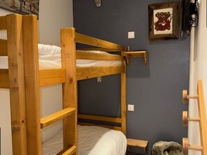 A bunk bed with a wooden frame, a small wooden stool, and a framed picture on the wall. - Apartment with balcony, mountain view - 6 guests (Les Saisies)