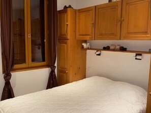 A bedroom with a single bed, wooden wardrobe, and a window with curtains. - Apartment with balcony, mountain view - 6 guests (Les Saisies)