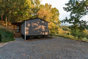 A small, single-story building with a sloped roof, a front porch, and a gravel driveway. - Hop Inn Private Hot Tub Fire Pit Mtn Views (Waynesville)