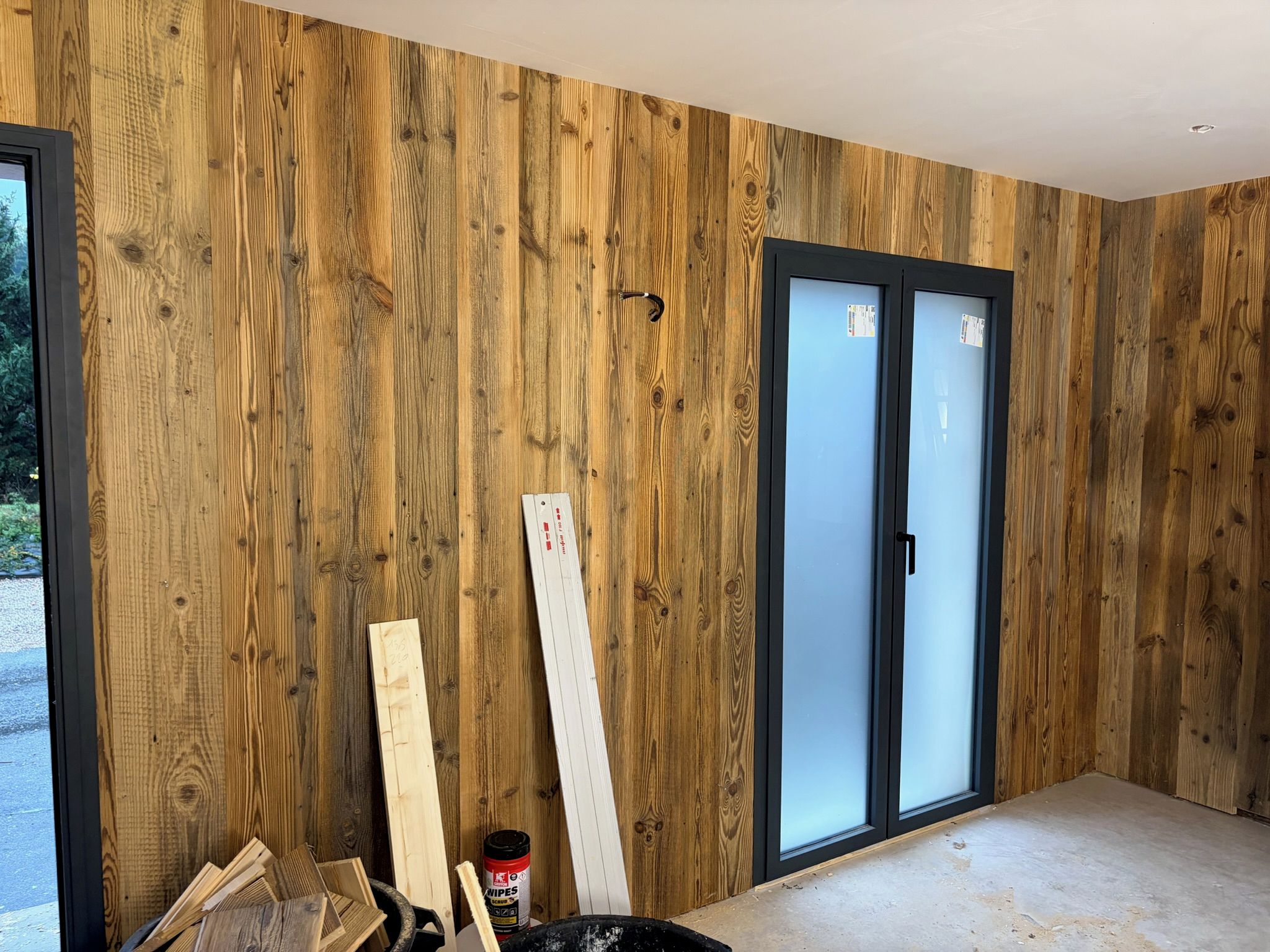 A room with wooden panel walls, a sliding glass door, and construction materials.