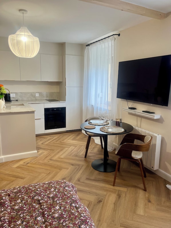 A modern kitchen with a dining area, a flat-screen TV, and a large window with curtains.