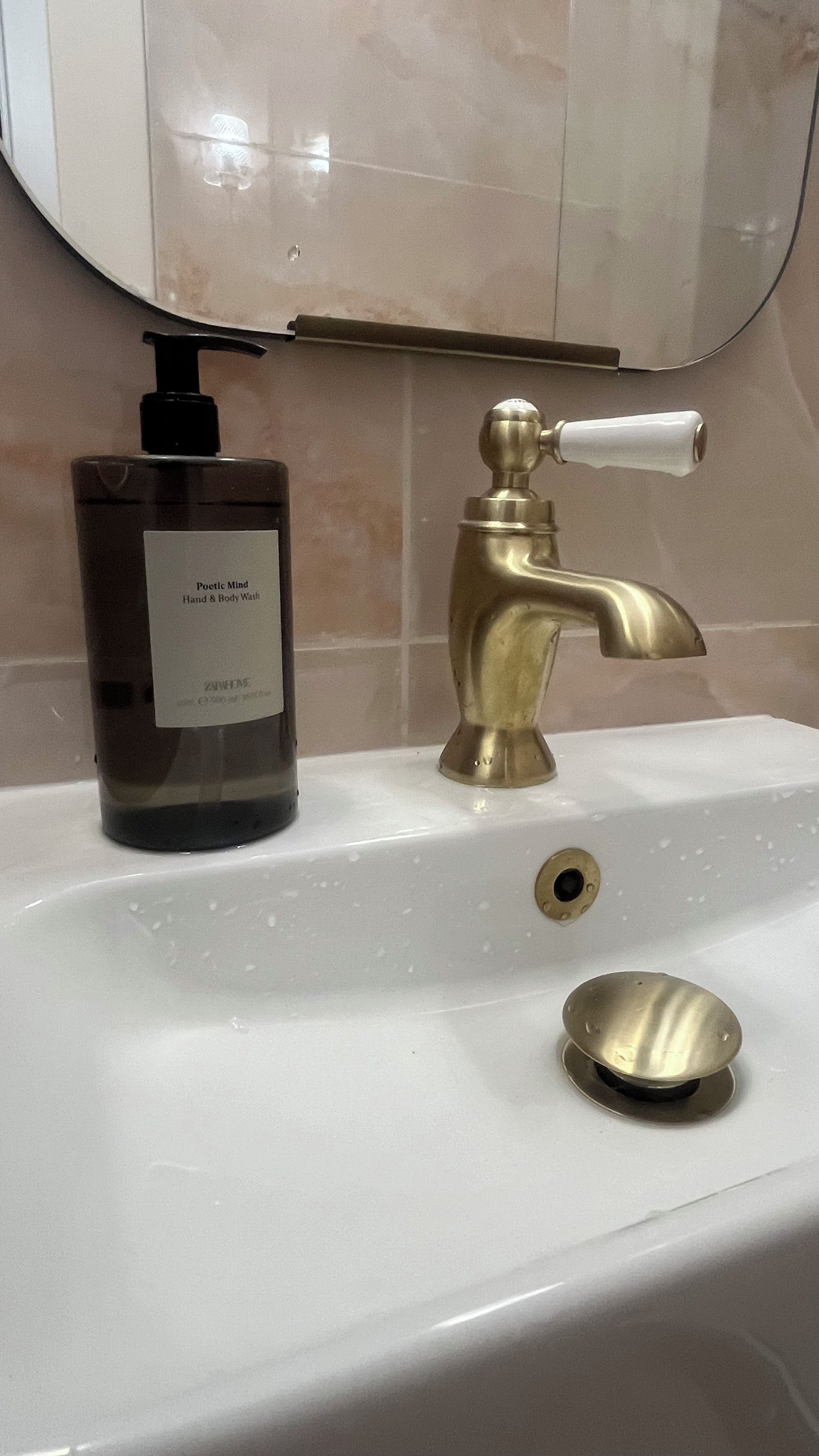 A bathroom sink with a gold faucet, a soap dispenser, and a mirror above.