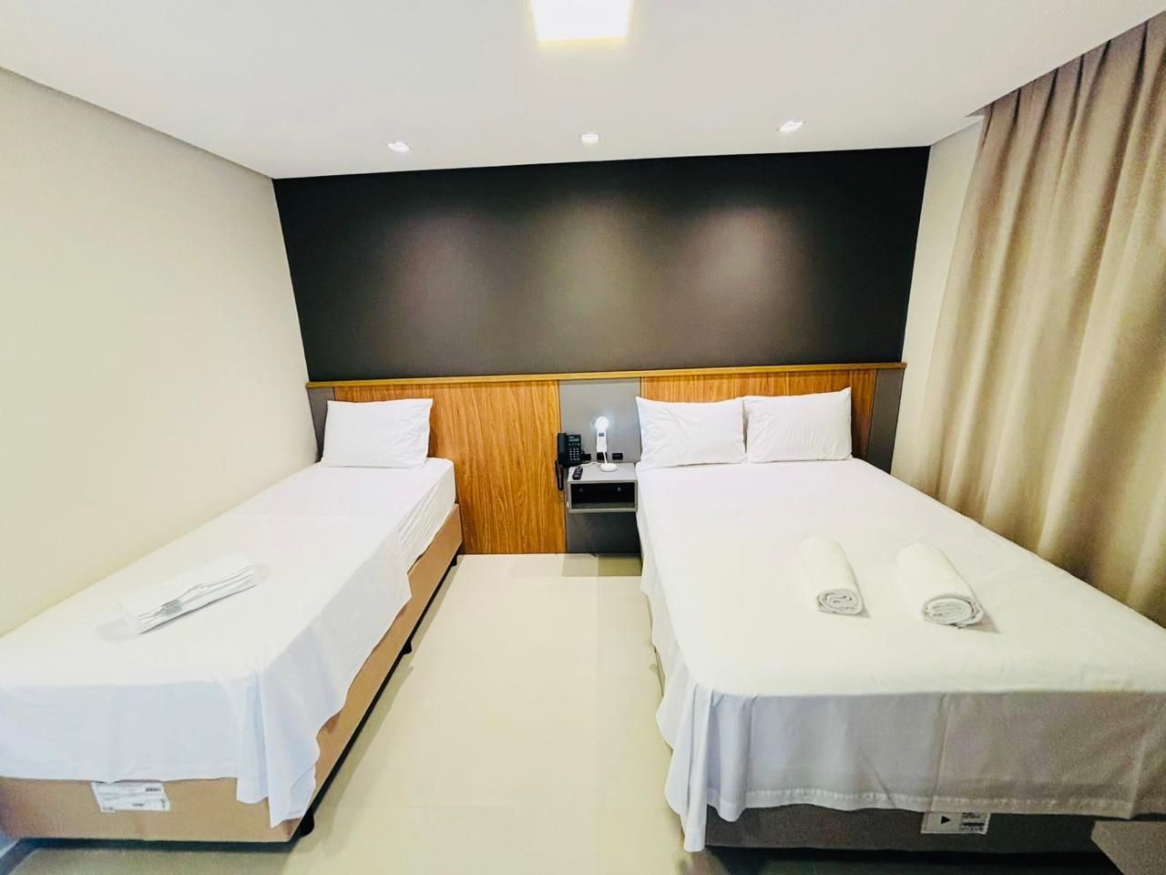 Een hotelkamer met twee eenpersoonsbedden, een nachtkastje met een lamp en een neutraal kleurenpalet.
