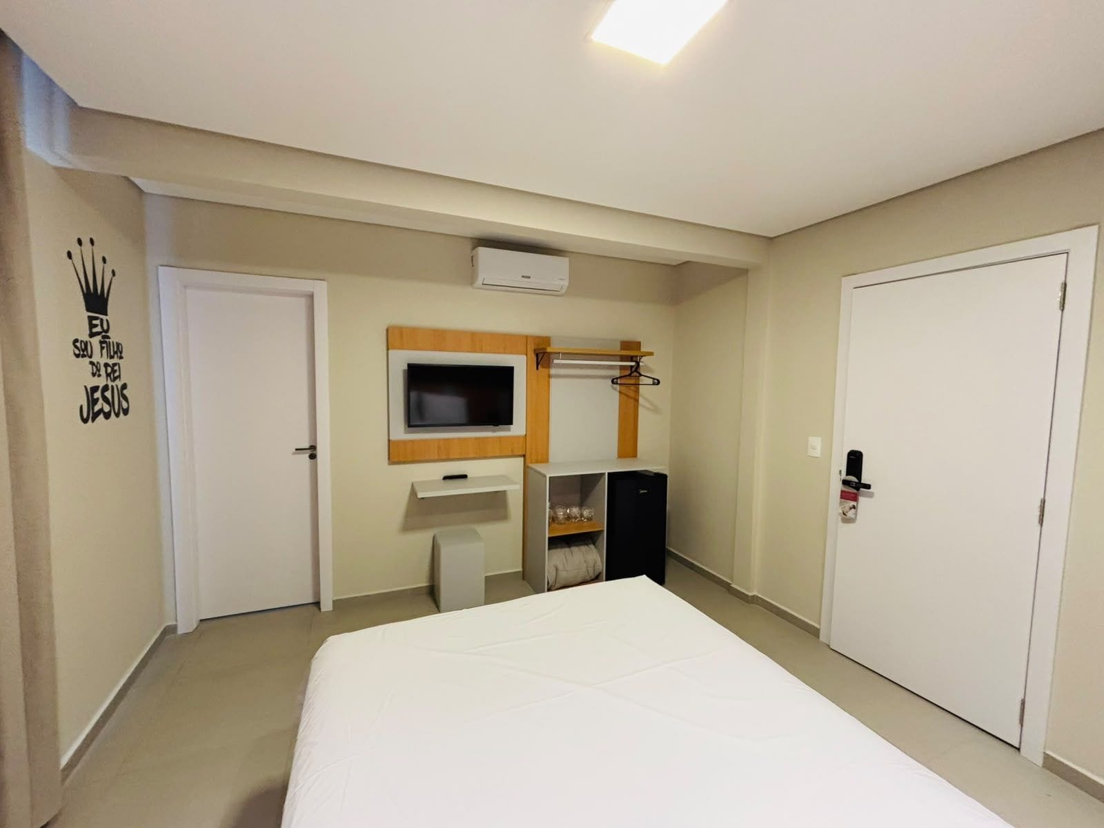 Ein Hotelzimmer mit einem Bett, einem an der Wand befestigten Fernseher, einem kleinen Schreibtisch mit Spiegel und einem Kleiderschrank.