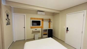 Ein Hotelzimmer mit einem Bett, einem an der Wand befestigten Fernseher, einem kleinen Schreibtisch mit Spiegel und einem Kleiderschrank.