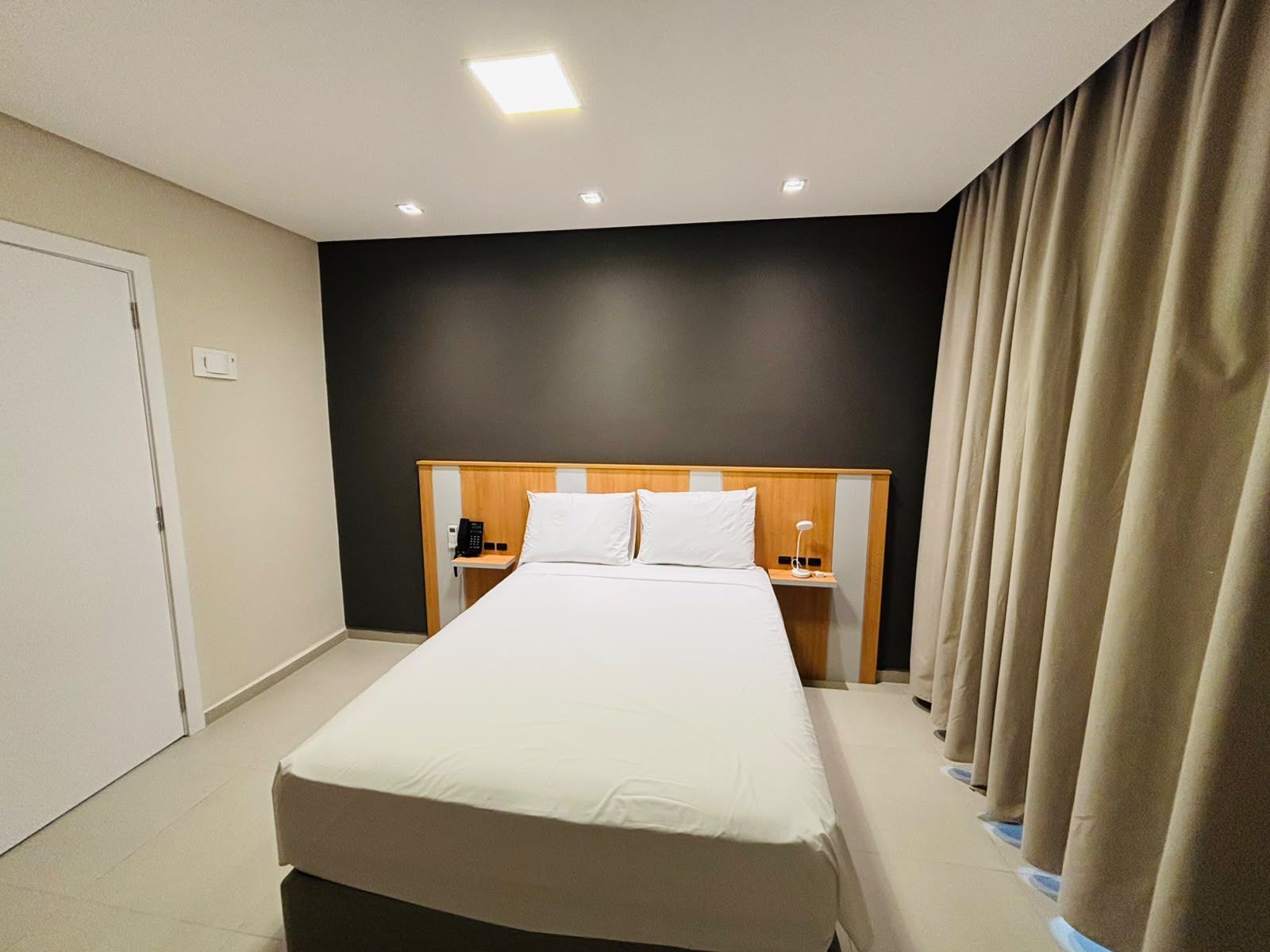 Une chambre d’hôtel avec un grand lit, des tables de chevet, un téléphone et un rideau.