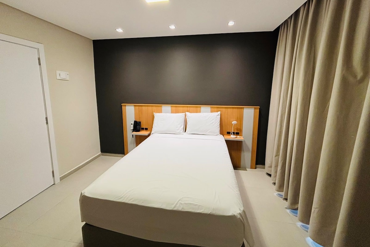 Una habitación de hotel con una cama grande, mesitas de noche, un teléfono y una cortina.