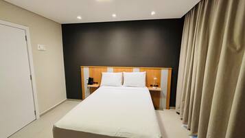 Une chambre d’hôtel avec un grand lit, des tables de chevet, un téléphone et un rideau.