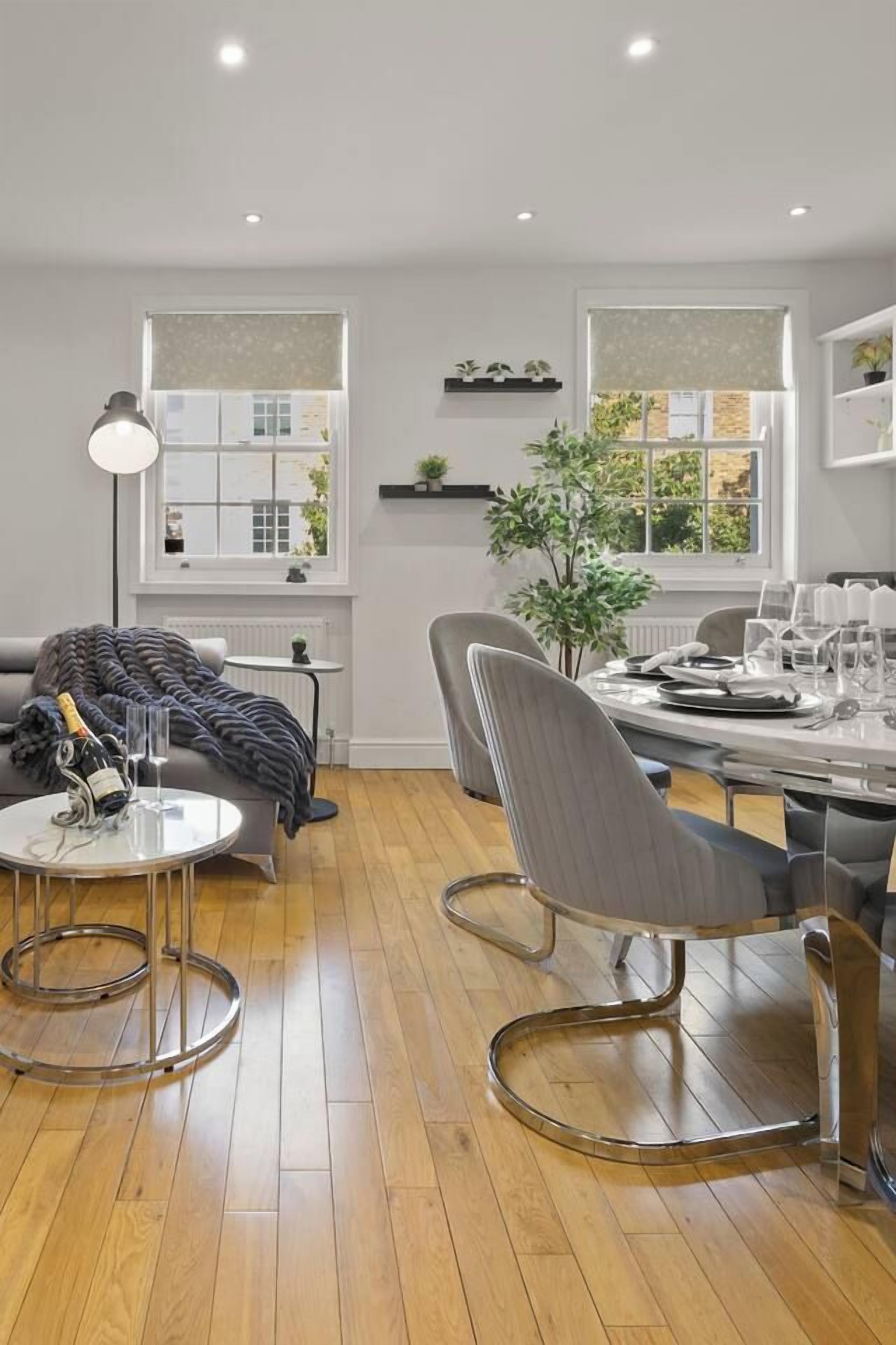 A modern living room with a dining area, wooden flooring, and large windows with blinds.