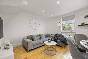 Ein modernes Wohnzimmer mit einem grauen Sofa, einem runden Couchtisch und einer Wanduhr.