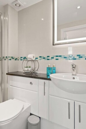 Ein modernes Badezimmer mit Toilette, Waschbecken mit Spiegel und Mülleimer.