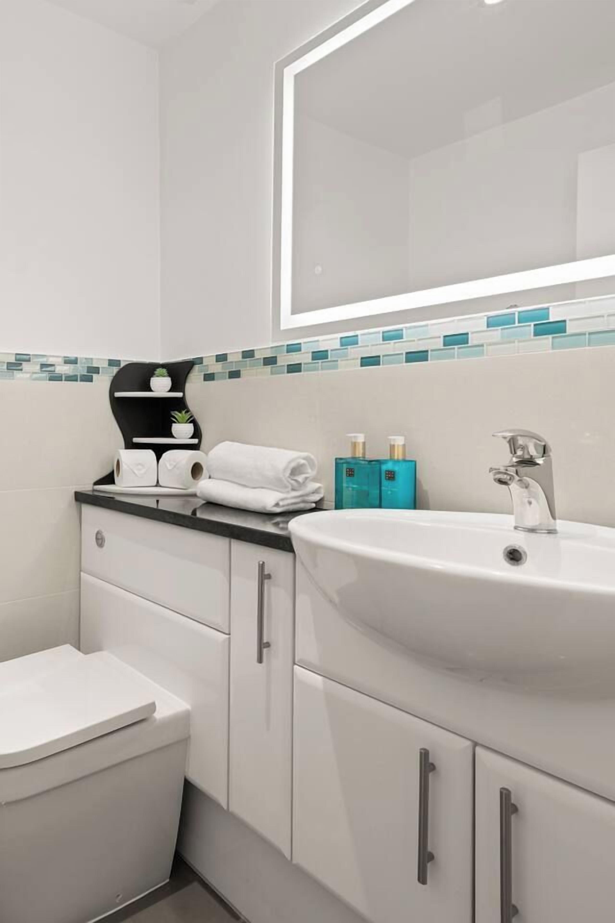 A modern bathroom with a white sink, a mirror, and a toilet. There are toiletries on the counter.