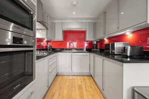 A modern kitchen with stainless steel appliances, white cabinetry, and a red accent wall. - Elegant 3bed Residence Marylebone & Paddington (Greater London)