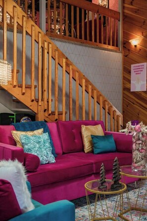 Una escalera de madera que lleva a un nivel superior, un sofá rosa con cojines decorativos y una mesa de vidrio con adornos con forma de árbol.