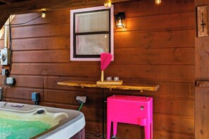 A wooden cabin interior with a hot tub, a pink cabinet, a shelf with glasses, and a framed window. - Dolly Vibes|Private|Hot Tub|Karaoke|Beauty Room (Sevierville)