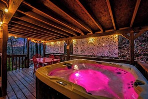 Un bain à remous avec éclairage rose, une terrasse en bois et un espace salon extérieur.