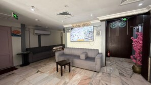 Um hall de entrada com sofá, mesa pequena, televisão na parede e relógio.