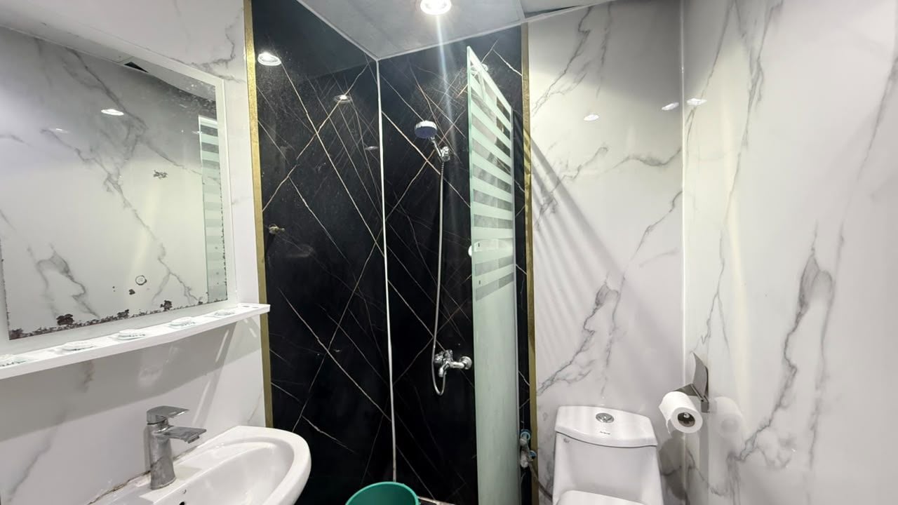 A bathroom with a white sink, a mirror, a black tiled shower enclosure, and a toilet.