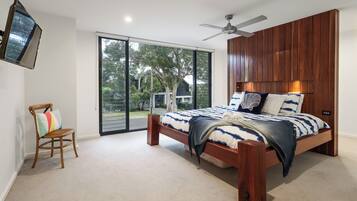 A bedroom with a large bed, a wooden headboard, a ceiling fan, and a sliding glass door leading to a balcony.