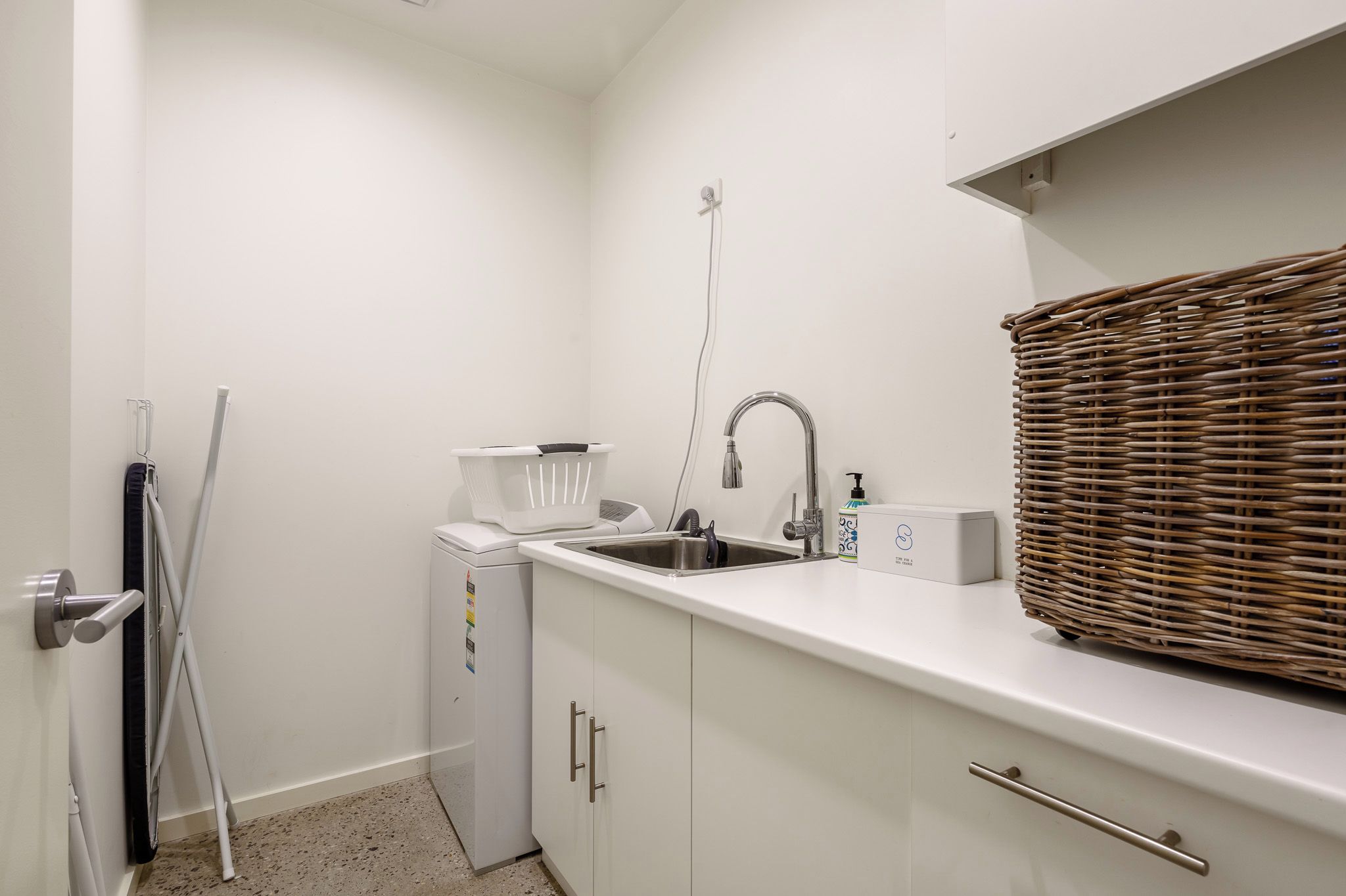 A compact kitchenette with a built-in washing machine, a sink, and a wicker basket.