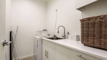 A compact kitchenette with a built-in washing machine, a sink, and a wicker basket.