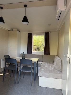 Habitació compacta amb taula de dinar, cadires, sofà i finestra amb cortines.