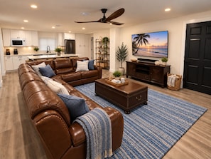 A modern living room with a brown leather sectional sofa, a coffee table, and a flat-screen TV mounted on the wall. - Sugarloaf Hideaway | Pool, Bikes, Kayaks, Paddleboards & Fishing Gear (Summerland Key)