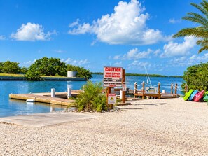 A waterfront dock with a caution sign warning of a slippery ramp, a boat launch area, and colorful kayaks.