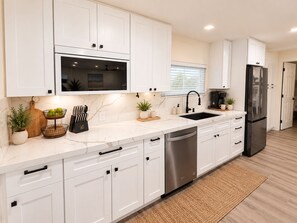 A modern kitchen with white cabinets, a stainless steel dishwasher, and a black refrigerator. - Sugarloaf Hideaway | Pool, Bikes, Kayaks, Paddleboards & Fishing Gear (Summerland Key)