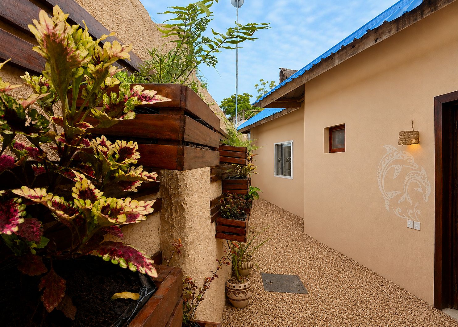 Un estrecho callejón con una jardinera de madera llena de plantas florecientes, un aplique de pared y una puerta con un emblema decorativo.