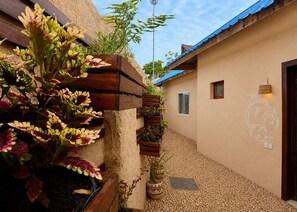 A narrow alleyway with a wooden planter filled with flowering plants, a wall-mounted light fixture, and a door with a decorative emblem. - Ocean Breeze Boutique Hotel (Nungwi)