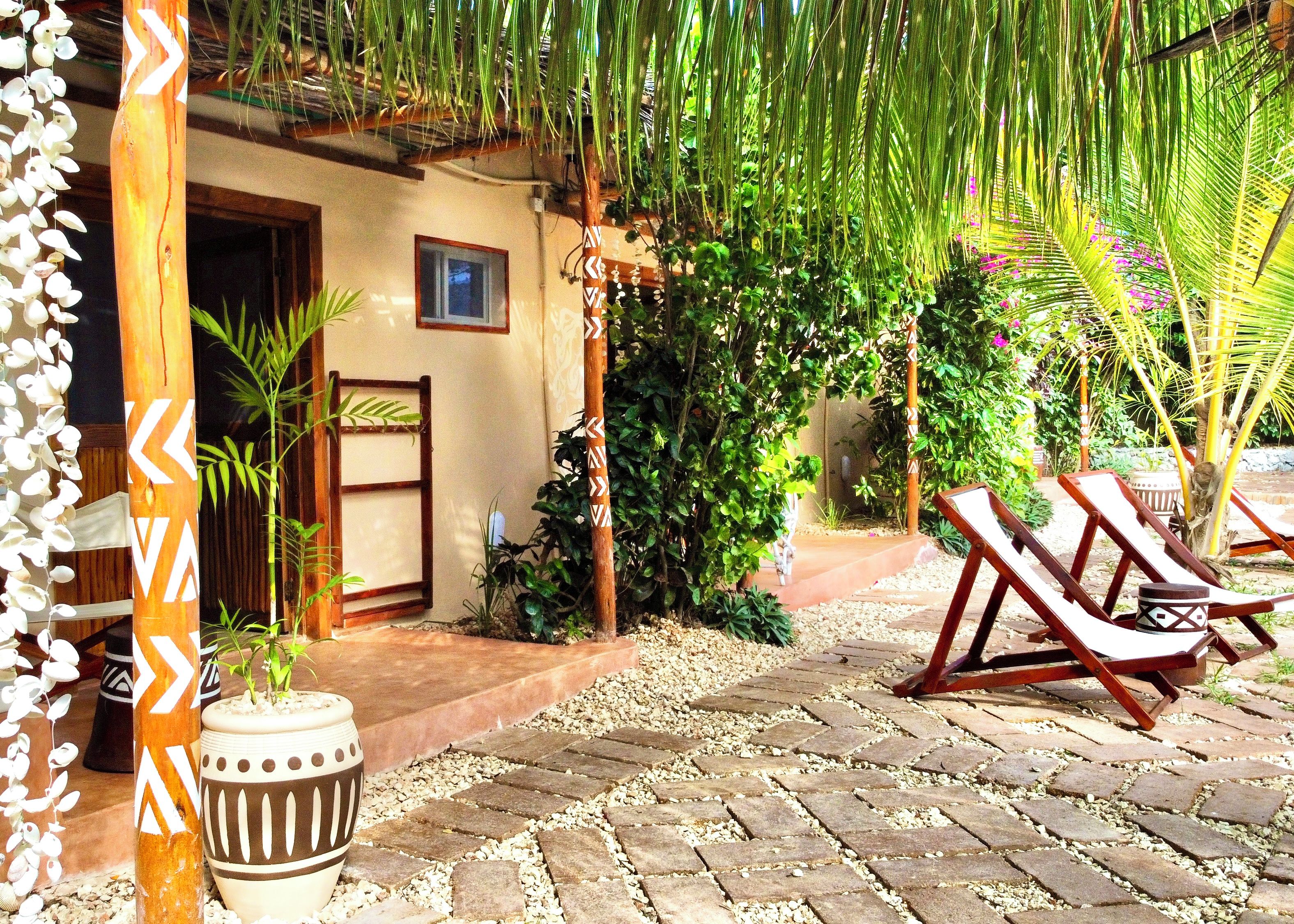 Un espacio al aire libre tropical con un camino, sillones de descanso y plantas en macetas.