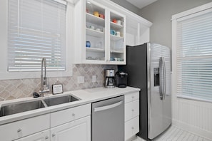 A modern kitchen with white cabinetry, a stainless steel refrigerator, a coffee maker, and a tiled backsplash. - Sugar Sand Cottage at Destin Pointe (Destin)