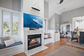 A spacious living room with a fireplace, a large flat-screen TV, and a dining area with a kitchen in the background. - Sugar Sand Cottage at Destin Pointe (Destin)