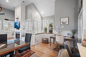 A spacious living area with a wooden floor, a glass-top dining table, and a fireplace. - Sugar Sand Cottage at Destin Pointe (Destin)