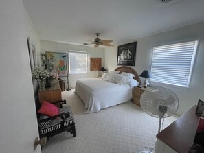 A bedroom with a bed, bedside tables, a fan, a desk, and a window with blinds. - The Scotch Bonnett Beach House - Best Location! (Nags Head)