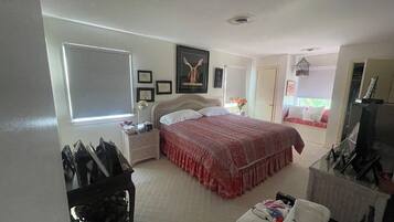 A bedroom with a bed, bedside table, dresser, and a window with blinds.